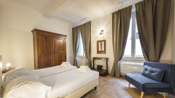 A bedroom with a large bed, a wooden wardrobe, a small table with a lamp, and a blue sofa. - Santa Croce Retreat by MMega (Florence)