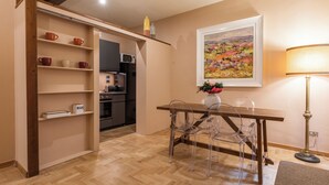 A compact kitchen with wooden shelves, a dining table with clear chairs, and a painting on the wall. - Santa Croce Retreat by MMega (Florence)