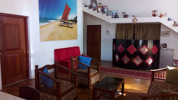 Una sala de estar con piso de madera, un sofá rojo, un sillón azul, una mesa de centro de vidrio y una escalera con pared de diseño rojo y negro.