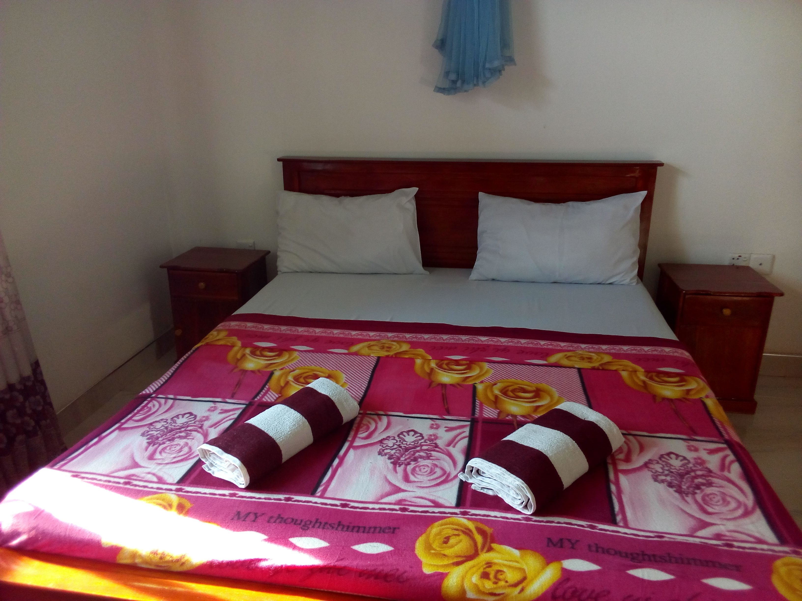 Una cama con una colcha estampada, dos almohadas blancas y dos toallas enrolladas.