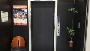 Ein Aufzug mit schwarzer Tür, einem Stuhl, einer Topfpflanze und einem Poster an der Wand.