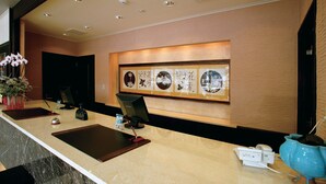 Ein Hotel-Rezeptionsbereich mit Marmor-Theke, einem digitalen Bildschirm, einer Vase mit Blumen und gerahmten Kunstwerken an der Wand.