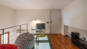 Una sala de estar moderna con una mesa de centro de vidrio, un reposapiés estampado, un televisor sobre un mueble bajo y un mueble de entretenimiento negro.