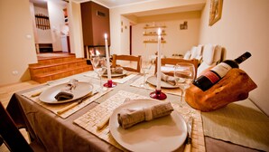 A dining table set with plates, cutlery, and glasses, with a bottle of wine on a wooden block.