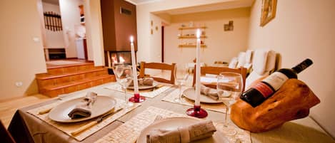 A dining table set with plates, cutlery, and glasses, with a bottle of wine on a wooden block.