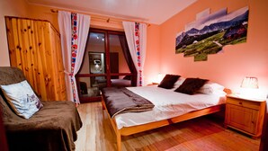 A cozy bedroom with a wooden bed, a chair, a nightstand, and a window with curtains.