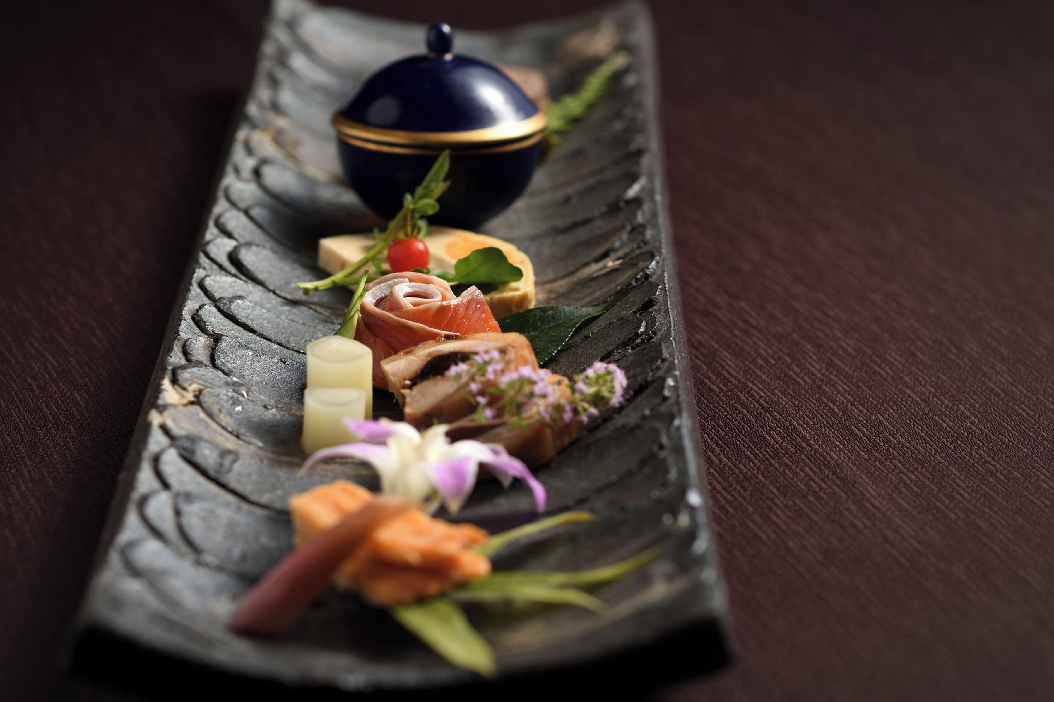 A rectangular slate serving tray with various food items and a decorative bowl.
