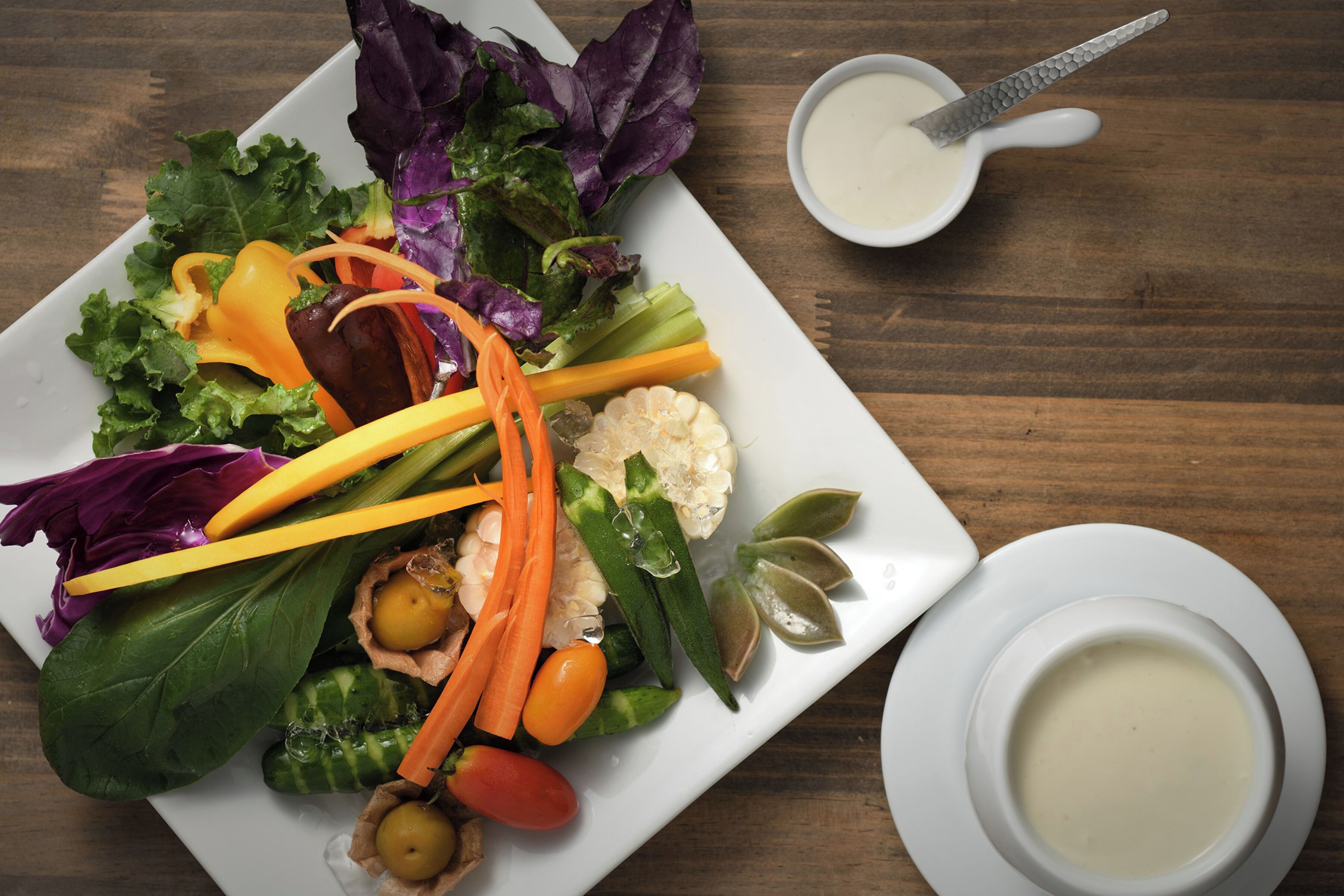 A white plate with a salad and a small bowl of dressing.