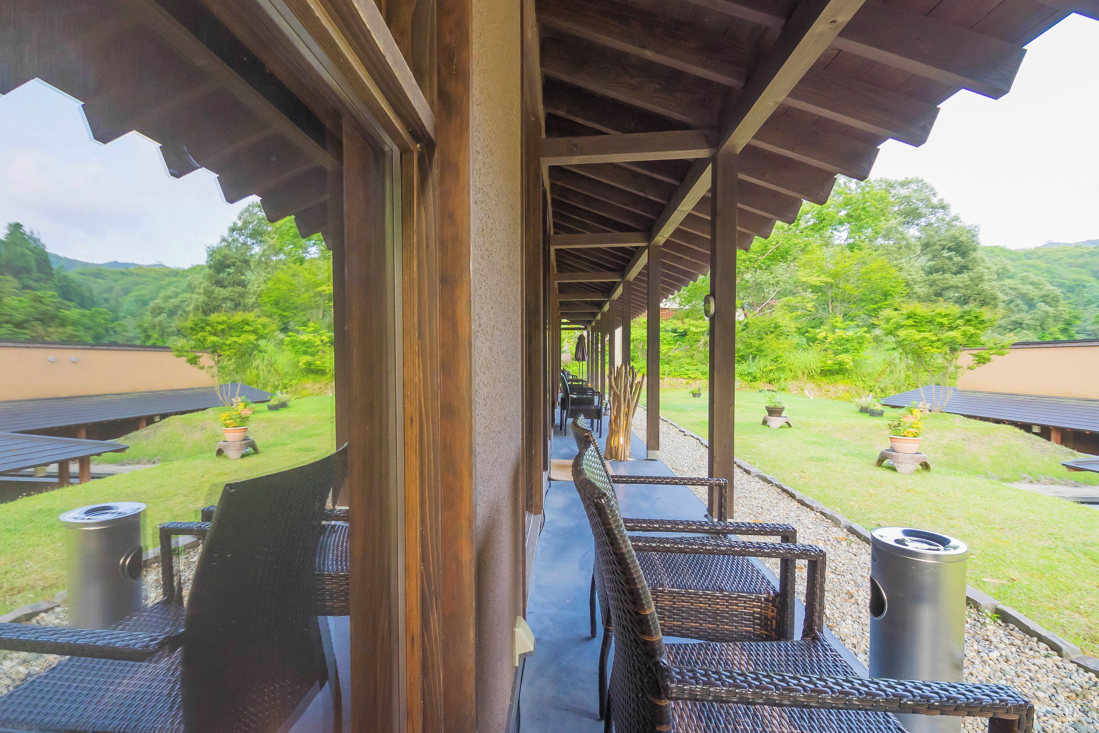 A covered outdoor seating area with wicker furniture and a view of a lush garden and mountains.
