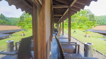 A covered outdoor seating area with wicker furniture and a view of a lush garden and mountains.