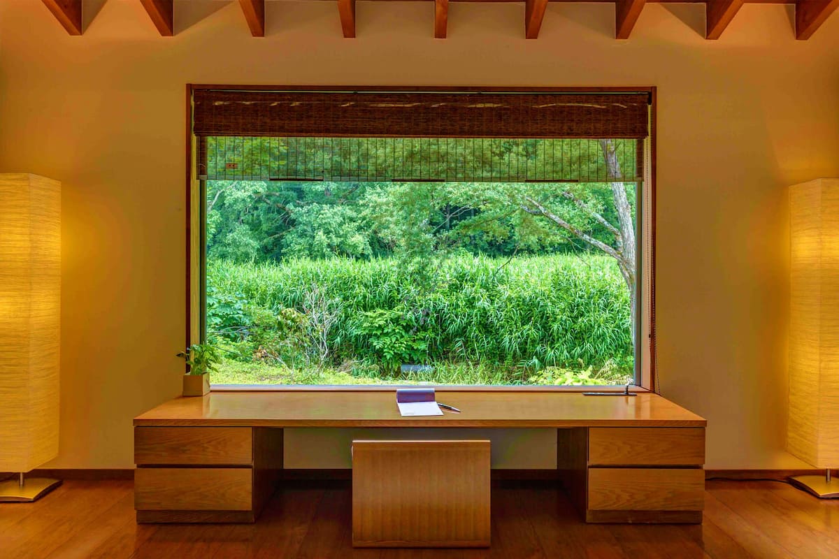 A wooden desk with a view of a lush garden through a large window.