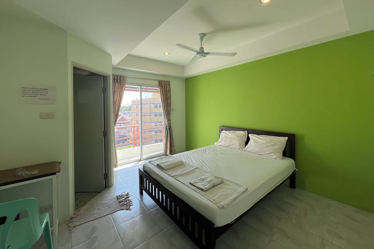 A bedroom with a bed, a ceiling fan, a view through a window, and a green wall.