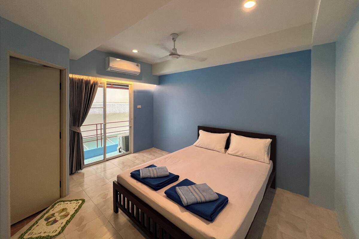 A bedroom with a bed, a ceiling fan, and a view of a balcony.