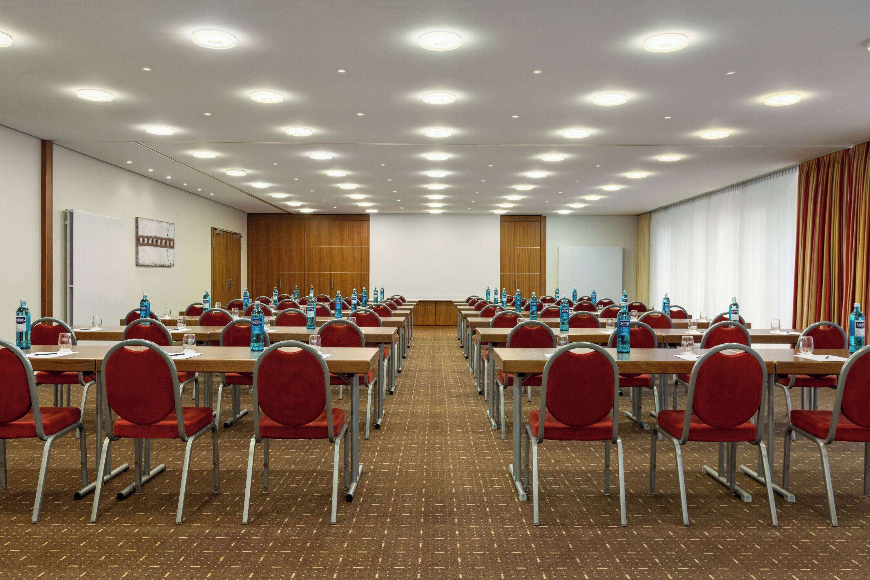 A conference room with rows of red chairs, tables, and water bottles.
