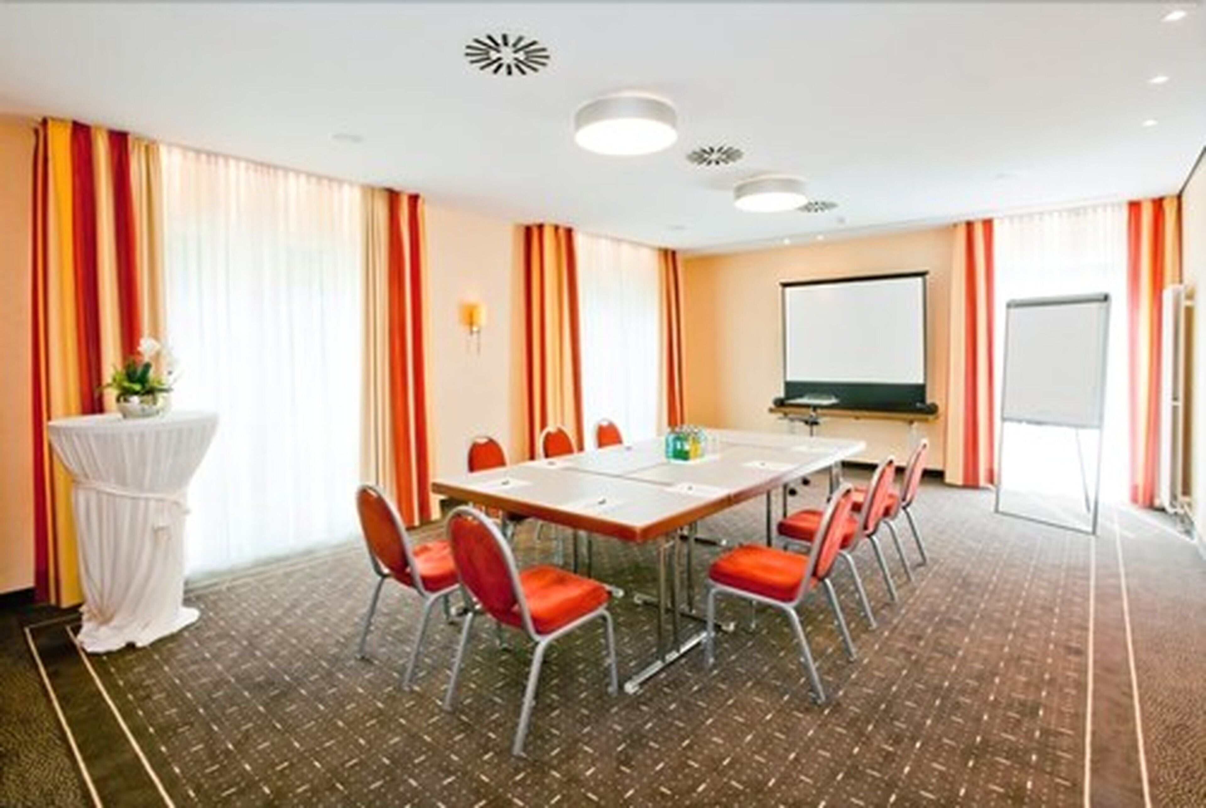 A conference room with a long table, red chairs, a whiteboard, and a projector screen.