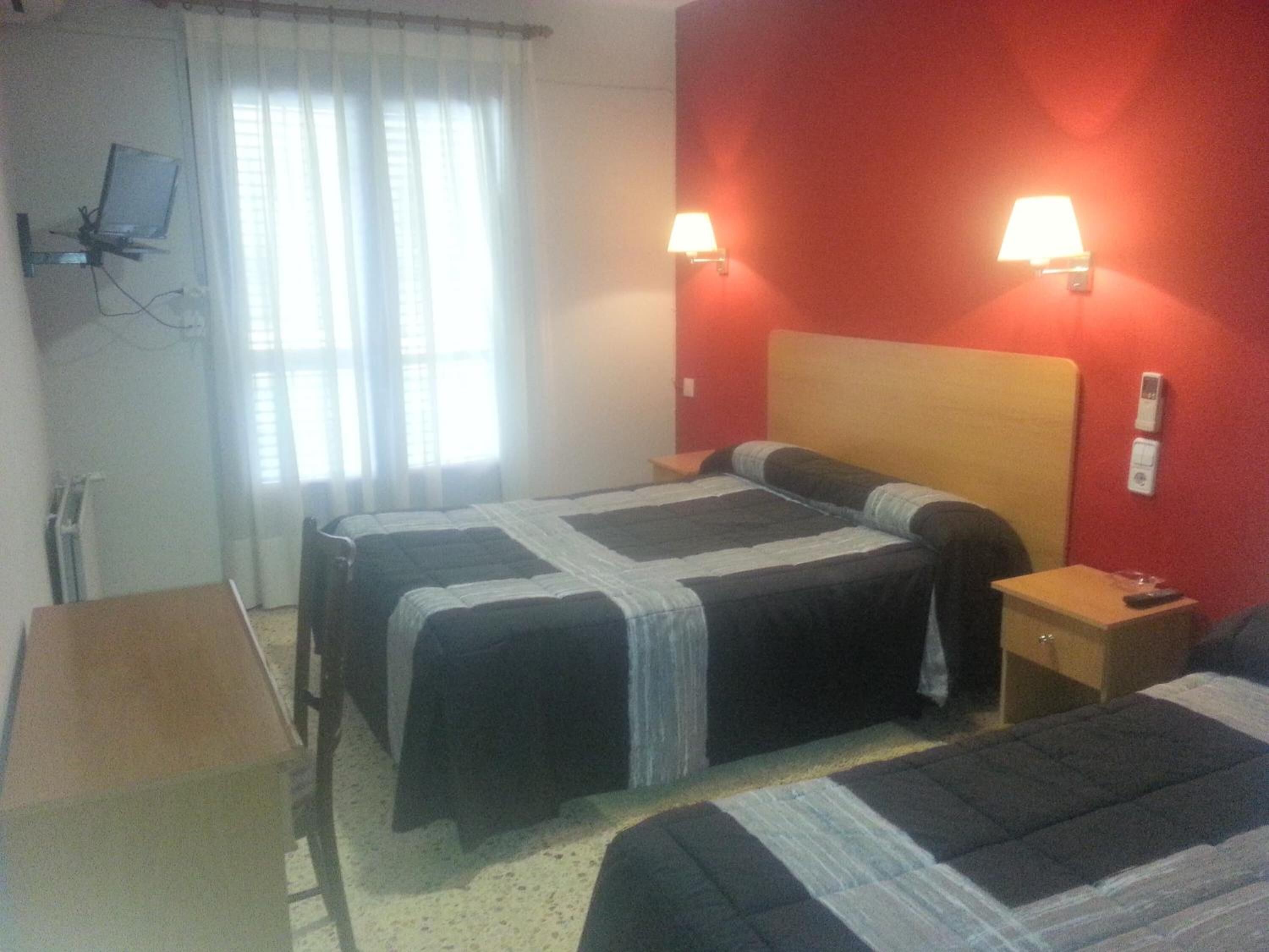 Habitación de hotel con dos camas, una pared roja y dos lámparas de pared.
