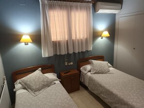 A bedroom with two single beds, a nightstand, a window with curtains, and wall-mounted lamps. - Hostal Cal Jaume (Mollerussa)