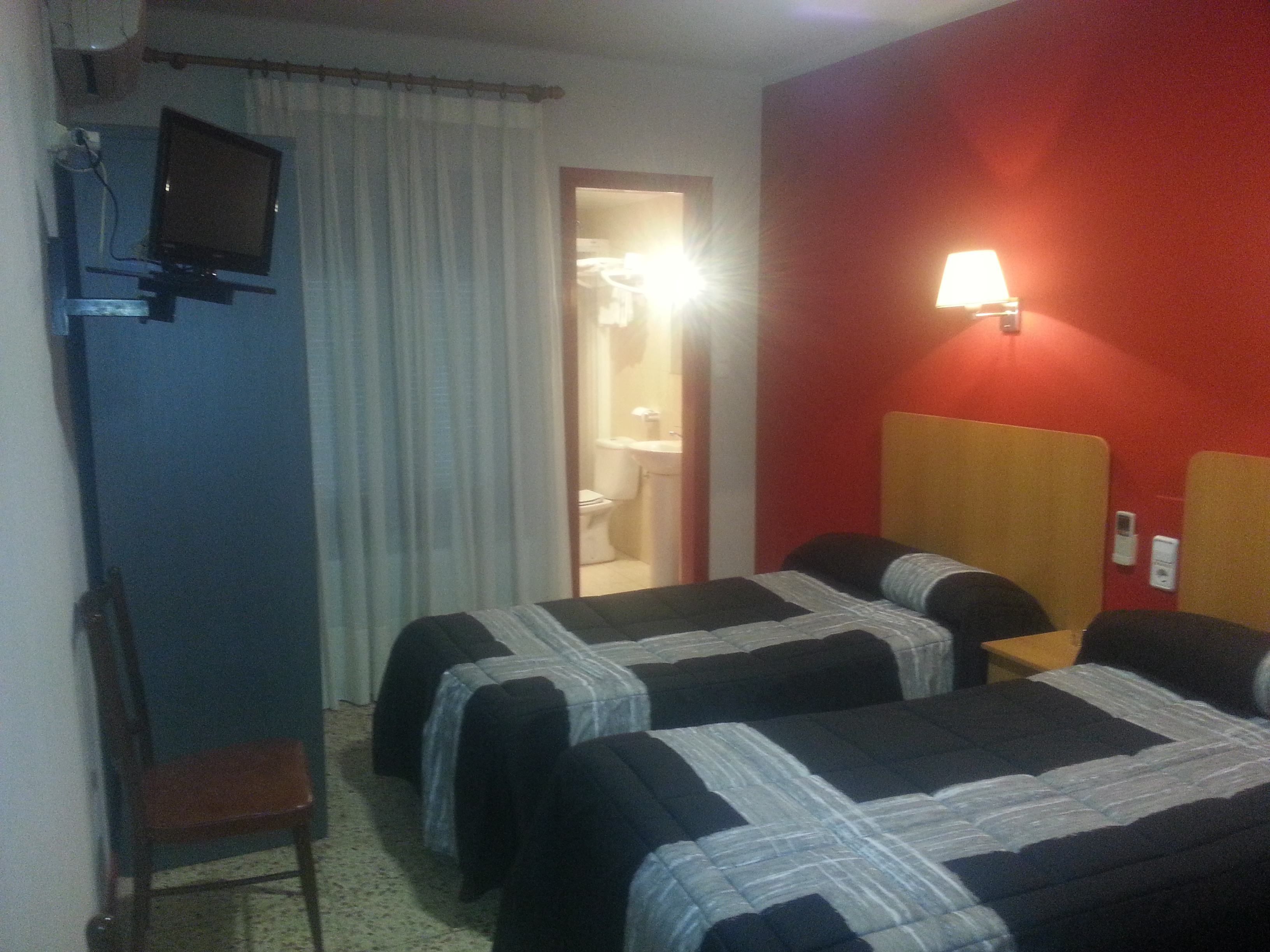 A hotel room with two beds, a TV, a chair, and a bathroom visible through an open door.