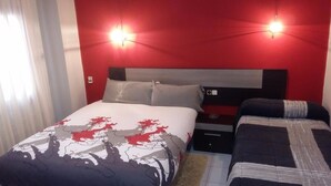 Ein Hotelzimmer mit roter Akzentwand, einem großen Bett mit gemustertem Überwurf, zwei Nachttischen und einem Beistelltisch.