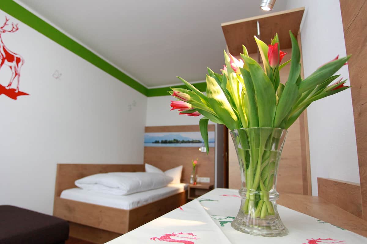 A hotel room with a bed, a small table with a vase of tulips, and a wall with a red deer decal.