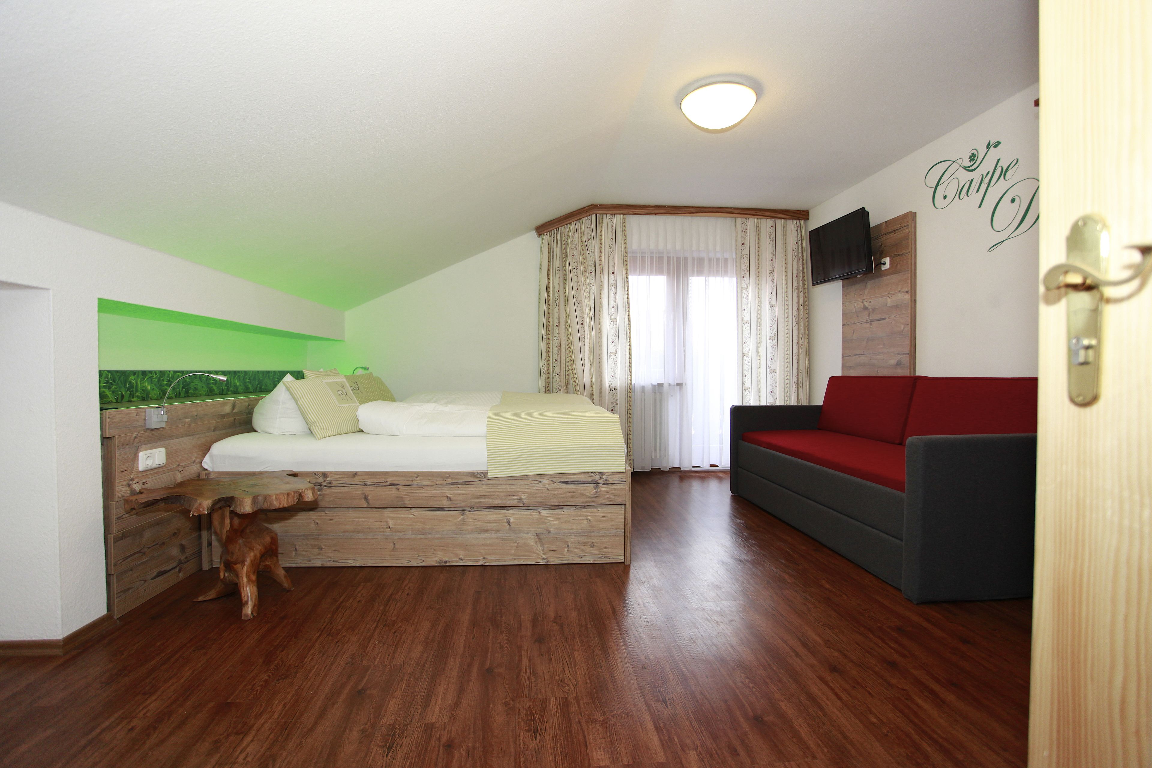 Un dormitorio con una cama, un sofá rojo, un cabecero de madera y un perro pequeño.