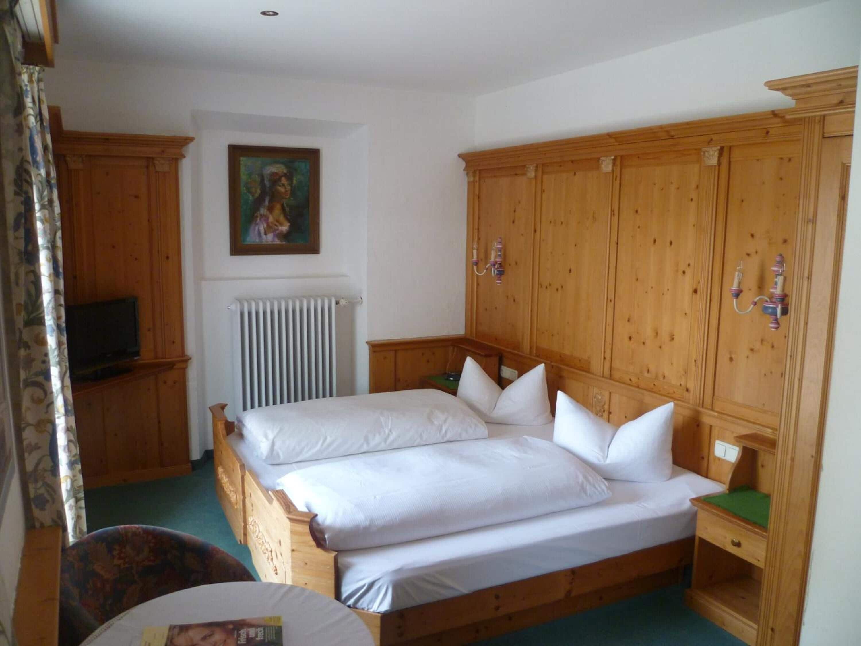 Une chambre à coucher avec un lit en bois, un radiateur, un téléviseur posé sur une commode et un tableau accroché au mur.