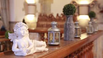 A statue of a cherub on a wooden shelf with decorative lanterns and a potted plant in the background.