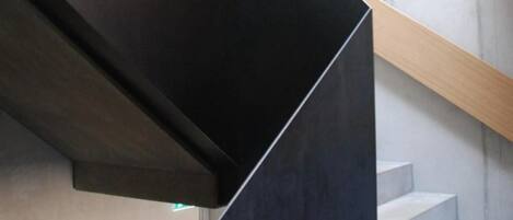 A modern staircase with a minimalist design, featuring dark and light grey steps and a wooden handrail.