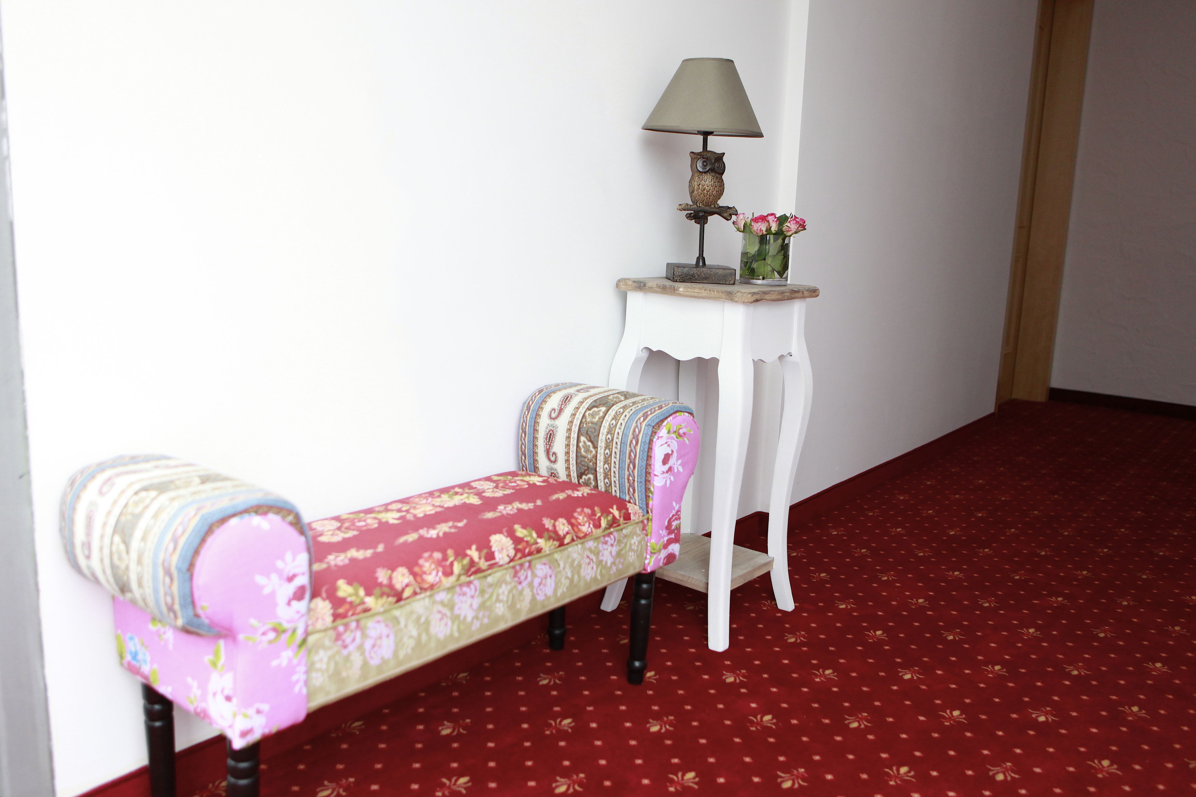 A small room with a bench and a table with a lamp and flowers.