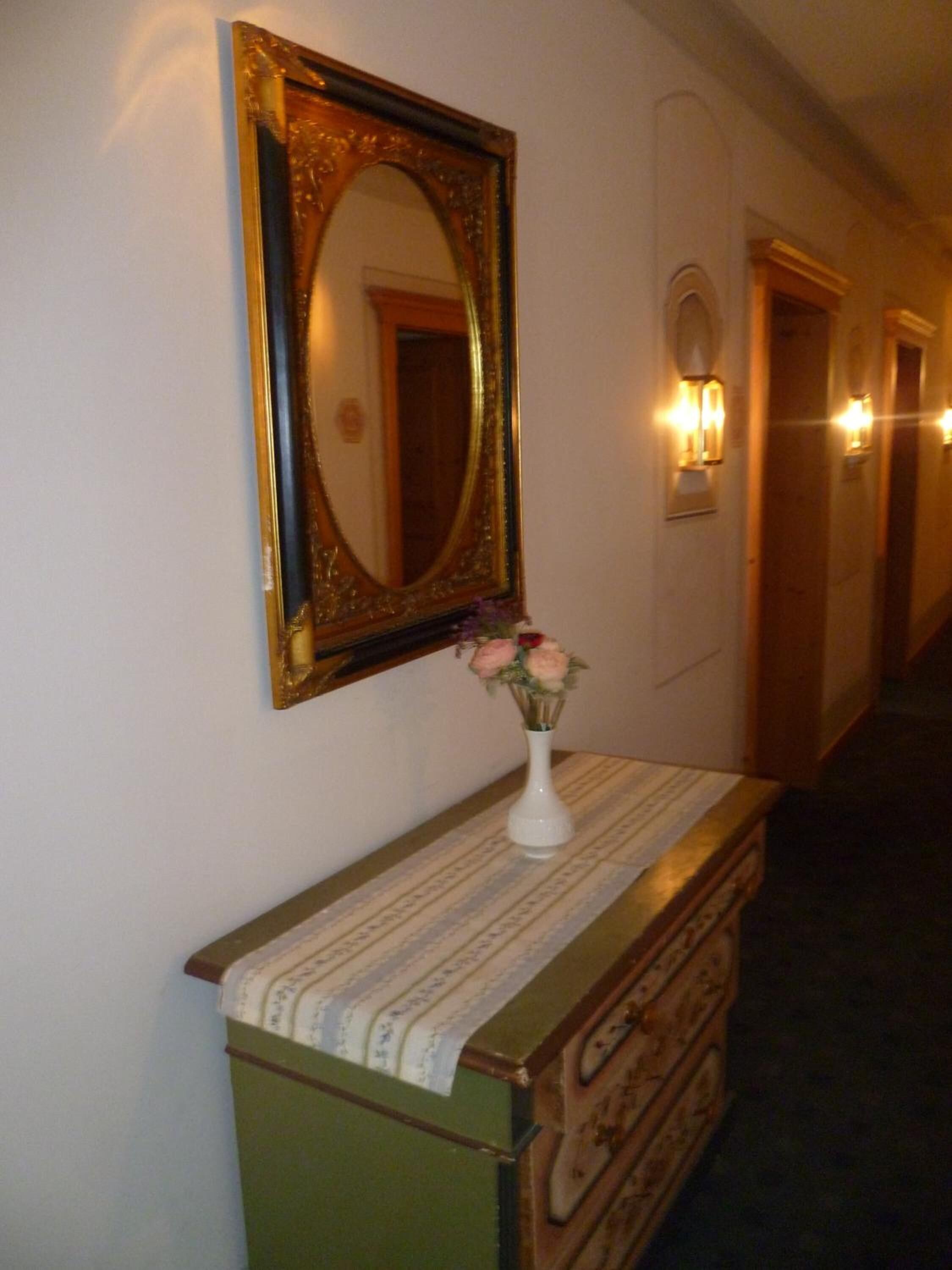 Un pasillo con un espejo, un florero con flores y apliques de pared.