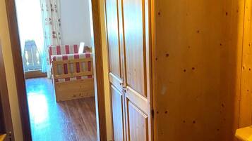 Un pasillo con suelo de madera, un armario de madera y un pequeño banco con cojín a rayas.
