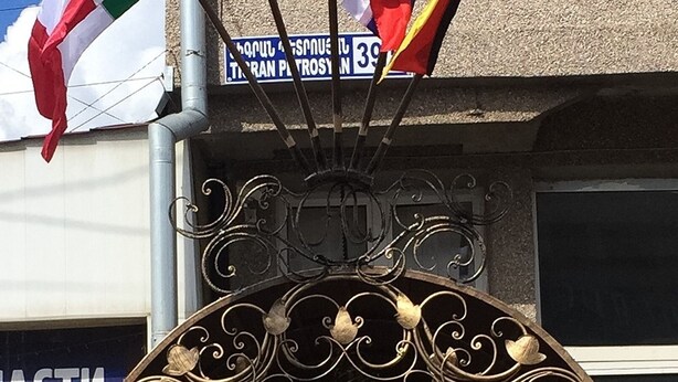A building entrance with a decorative archway, potted plants, and flags. - Apartments Tigran Petrosyan (Yerevan)