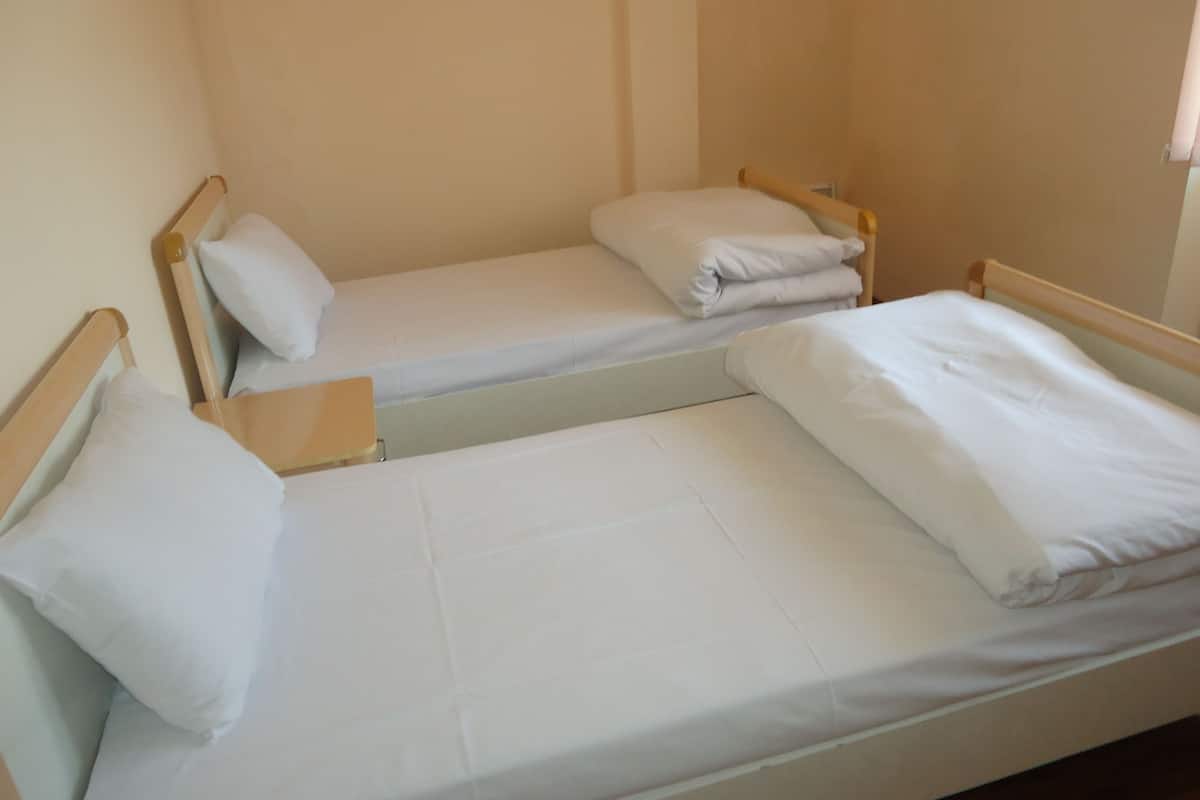Two single beds with wooden frames and white bedding in a room with plain walls and a window.
