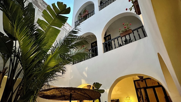 Un patio con zona de comedor, plantas en macetas y un edificio con varios balcones.