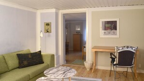 Una sala de estar con un sofá verde, una mesita redonda pequeña, una silla de mimbre y un escritorio de madera.