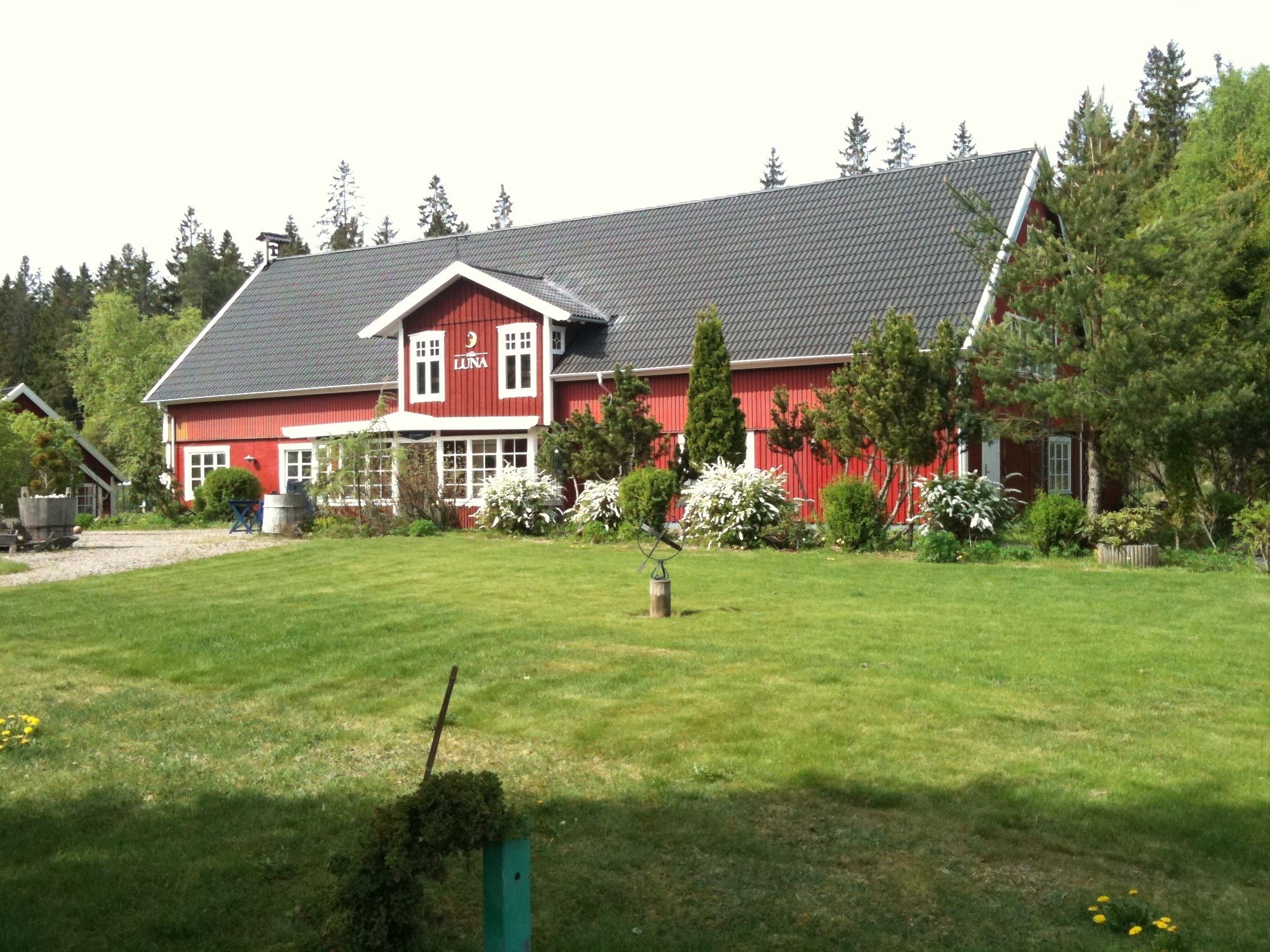 Ett rött hus med ett sluttande tak, omgivet av en välskött gräsmatta och träd.