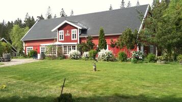 Ett rött hus med ett sluttande tak, omgivet av en välskött gräsmatta och träd.