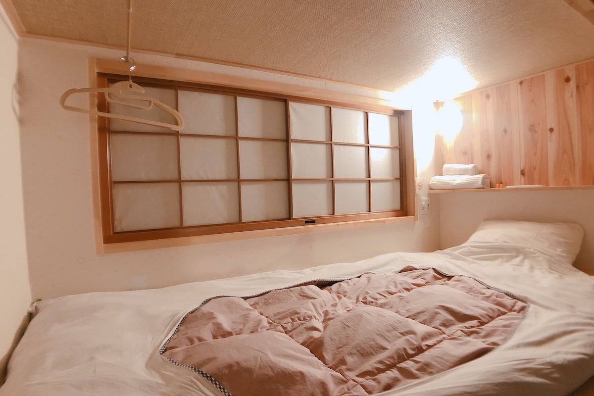A bedroom with a bed, a window with a wooden frame, and a shelf with towels.