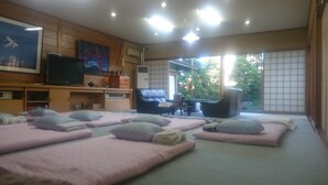 Una habitación con una mesa de masaje, un televisor y un amplio ventanal con vistas a árboles.