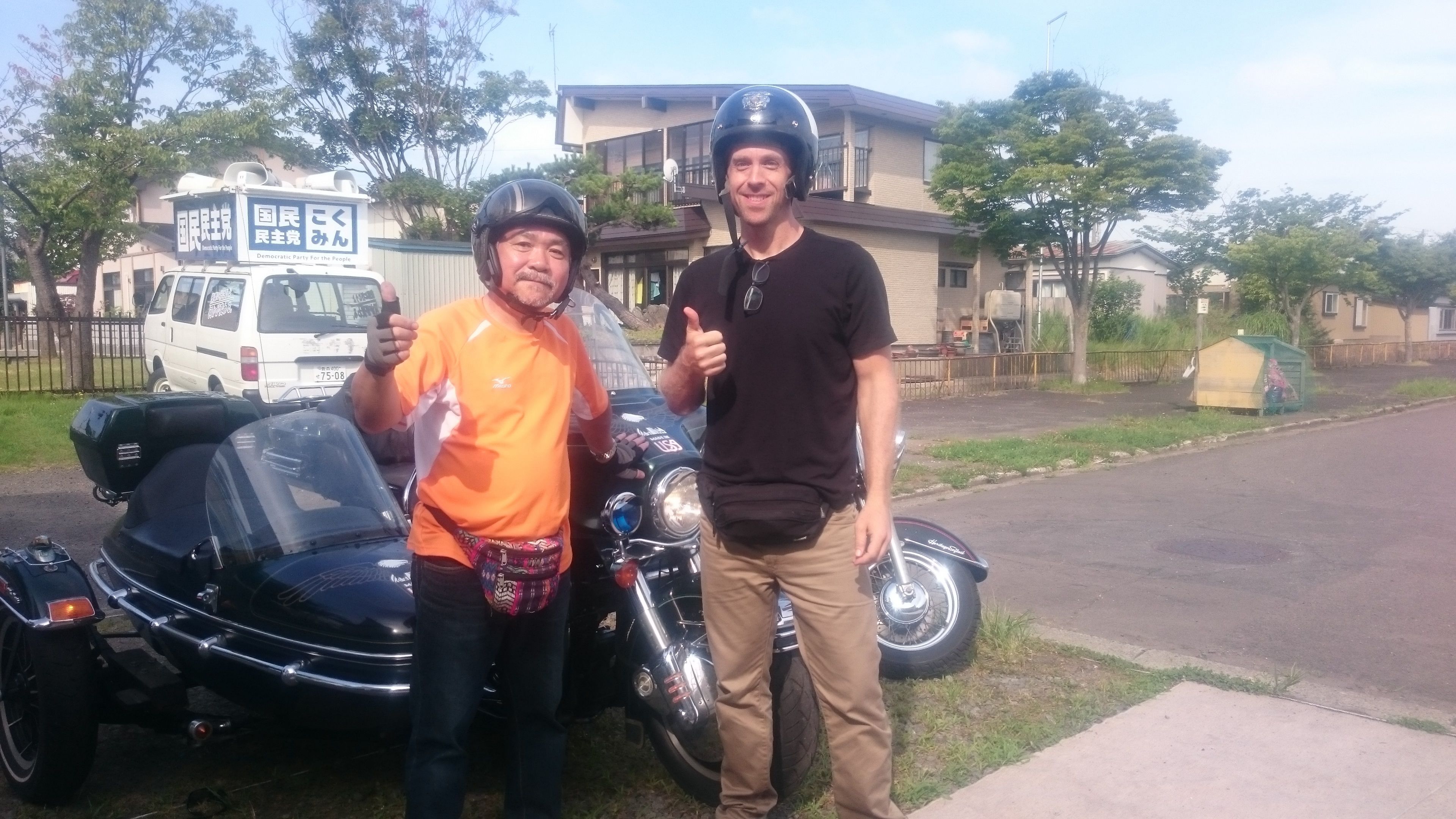 Two people standing next to a motorcycle and a white van with a sign in a residential area.