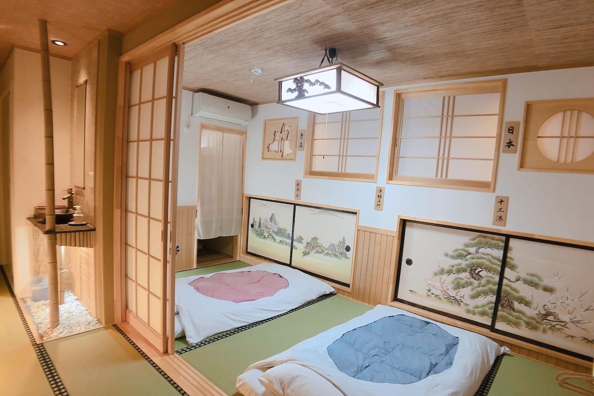 A traditional Japanese room with tatami flooring, two tatami beds, shoji screens, and artwork on the walls.