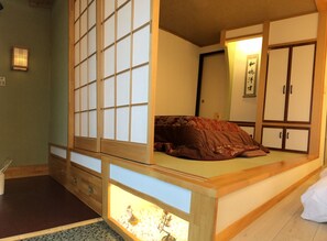 A traditional Japanese-style room with tatami flooring, a low wooden bed with a red blanket, a shoji screen, and a small indoor garden. - PittINN - Hostel (Goshogawara)