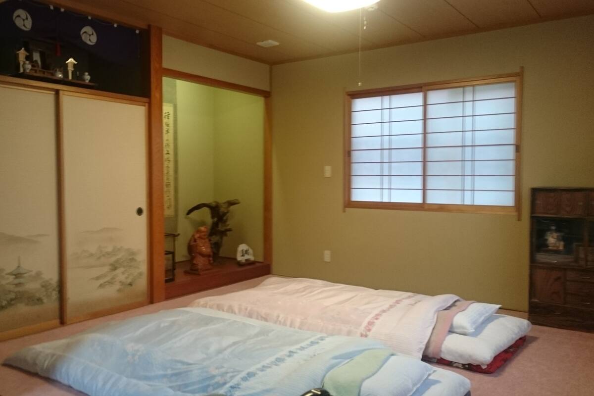 A traditional Japanese-style bedroom with tatami flooring, a futon bed, sliding doors, and a shoji screen window.