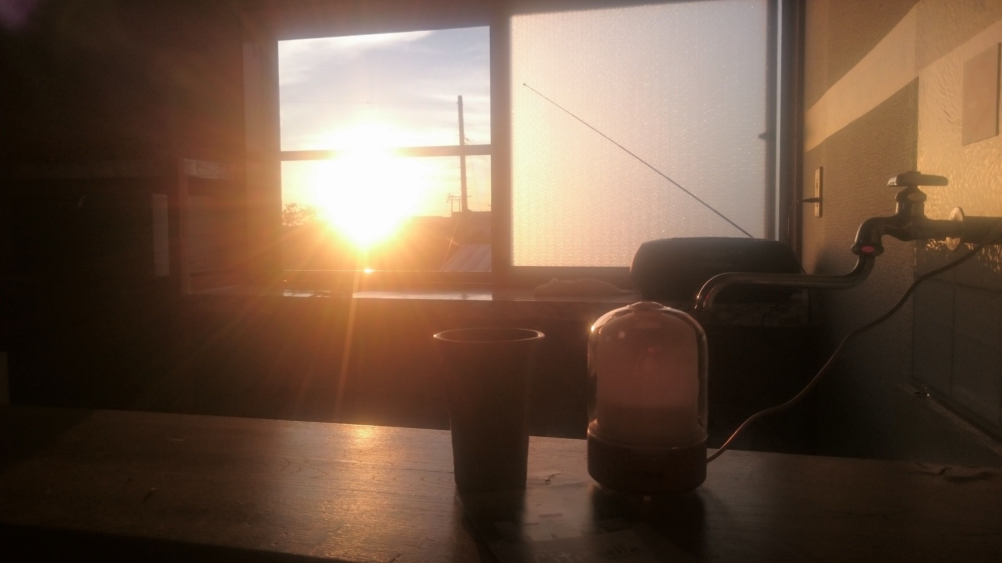 Een kamer met een raam dat uitkijkt op een gebouw, een tafel met een lamp en een wandmengkraan.