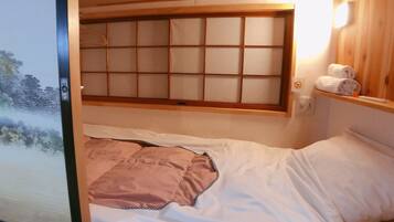 A room with a bed, a window with a wooden frame, and a towel rack with towels.