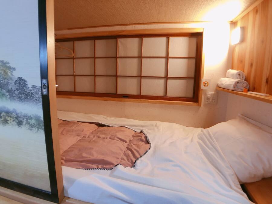 A room with a bed, a window with a wooden frame, and a towel rack with towels.