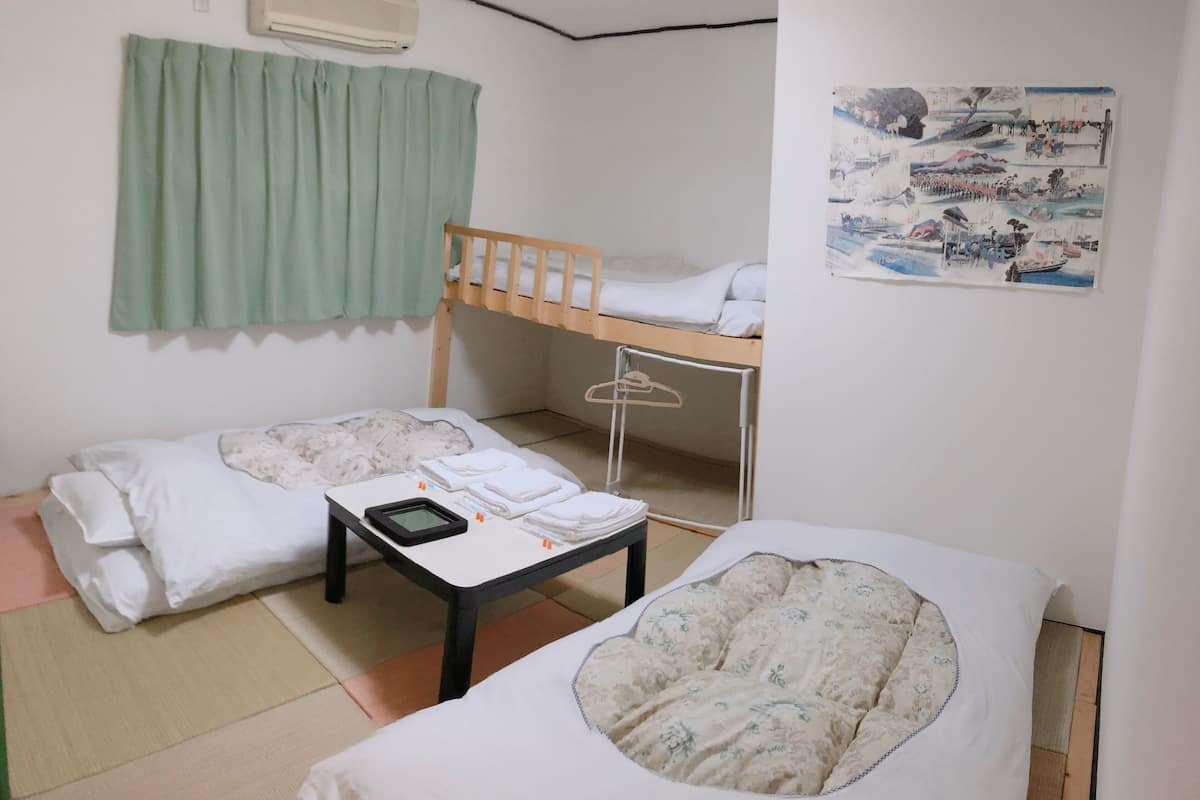 A dormitory room with two beds, a bunk bed, a small table with a tablet, a wall-mounted air conditioner, and a poster on the wall.