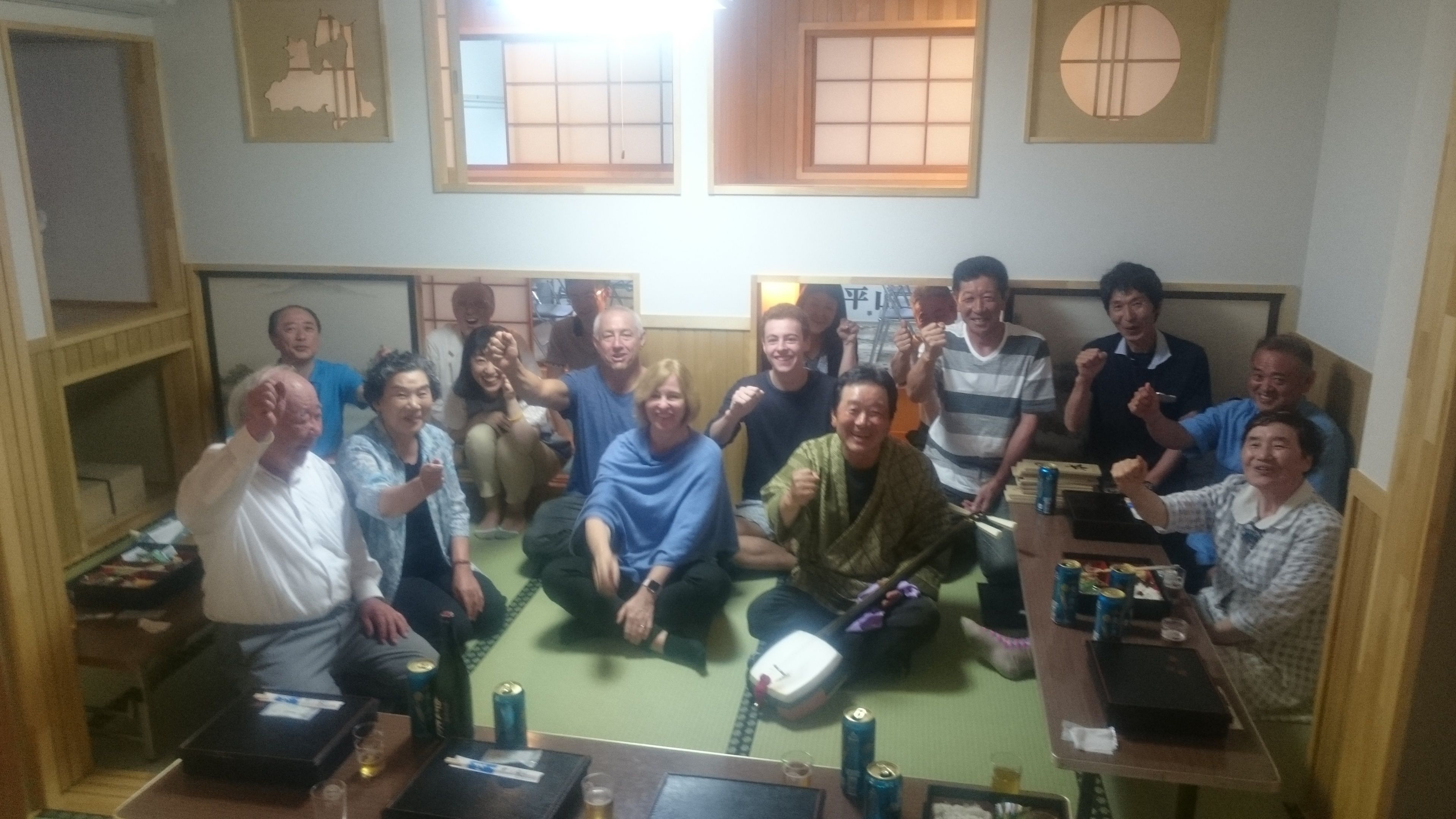 Un grupo de personas en una habitación con esteras de tatami, una mesa baja con bebidas y un tradicional biombó japonés shoji.