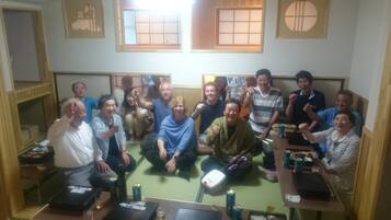 Un grupo de personas en una habitación con esteras de tatami, una mesa baja con bebidas y un tradicional biombó japonés shoji.