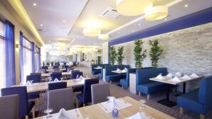 A modern restaurant with blue booths and tables, stone wall, and hanging pendant lights.